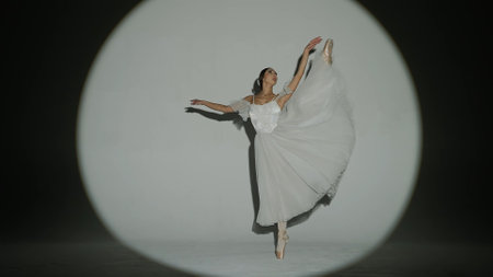 Portrait of female on white background in studio in bright spotlight. Elegant ballerina in white...