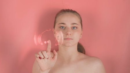 Young girl with bare shoulders without makeup on pink background. She is lying underwater and looking at the camera, resting her hand on the water or glass. At this time, waves form on the water.の写真素材