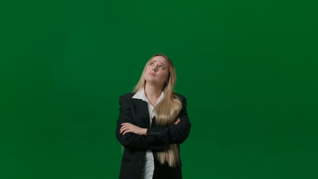 Portrait of female on chroma key green screen. Girl standing thinking hoping looking up but not finding idea, crossed hands, lamp lights up over head.の写真素材
