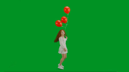 Little girl in white dress with red helium balloon on chroma key green screen isolated background...