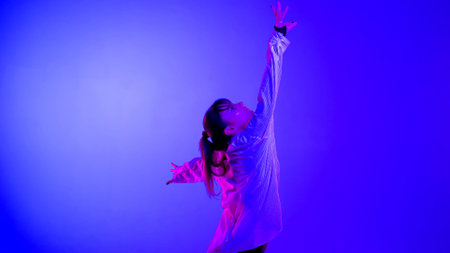 Young woman wearing a top, shorts and a shirt performing contemporary dance in studio. Neon blue, pink and red color scheme, ombre, gradient background. Medium sized.の写真素材