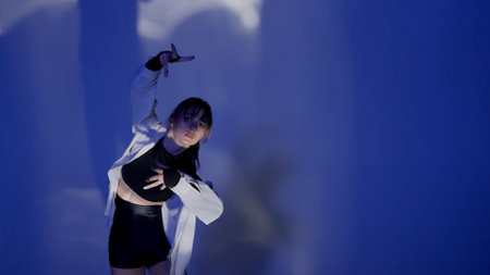 Young woman wearing a top, shorts and a shirt performing contemporary dance under the glare of light...