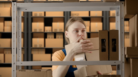 Business warehouse and logistics creative advertising concept. Portrait of a female model working in a warehouse. Uniformed warehouse girl lays on a shelf cardboard box .の写真素材
