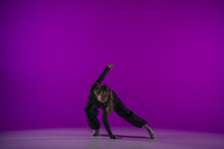 Energetic contemporary dance in purple studio light: young girl in black clothes shows grace and passion for dance. Full length. Promo or commercial.の写真素材