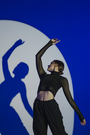 Girl in casual black clothes posing in studio on white background with blue spotlight. The dancer performs elements of contemporary choreography. Graceful movements.の写真素材