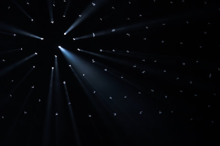 Rays of bright light come through holes in the black background of the studio. The rays cut through...