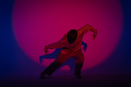 Guy in casual clothes dancing hip hop elements in studio with blue light. Dancer is in red circle of...