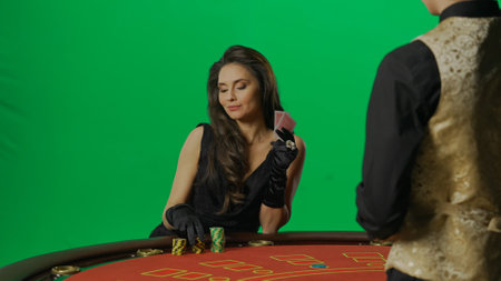 Gorgeous female in studio on chroma key green screen. Appealing woman in dress and man croupier at...
