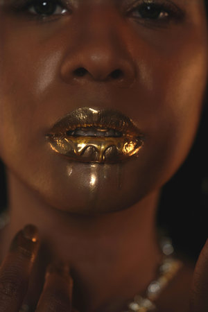 Portrait of a young African American woman with a gold necklace around her neck. Liquid gold is applied to the models lips and flows down in thin streams. Beauty concept. Close up.の写真素材