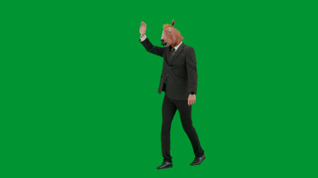 Man in business suit with horse head mask on green studio background. Businessman walking and waving hello. Concept of hard office work. Half turn.の写真素材