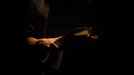 Studio shot of old retro hardcover book on dark background in warm light. Man holding big old dusty vintage book in hands.の写真素材