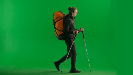 Tourist traveling using trekking poles on a hike. Full length man with backpack on his back walking on green screen. The concept of hiking. Side view.の写真素材