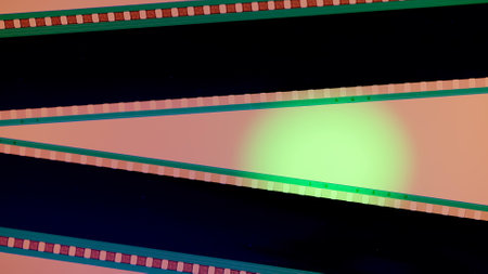 Two black film strips on pink background illuminated with green circular light, close up. Copy space.の写真素材