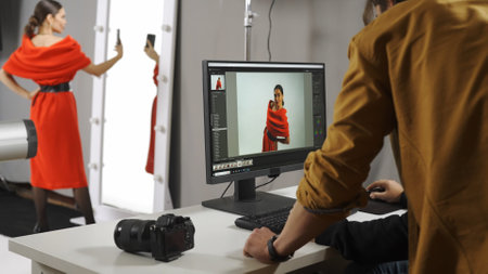 Backstage of model and professional team in the studio. Photographer and man editor talking looking at photos on monitor, woman model taking selfie.の写真素材