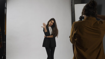 Backstage of model and professional team in the studio. Full length of attractive model in suit posing, photographer taking pics, cool expression.の写真素材