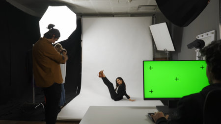 Backstage of model and professional team in the studio. Full shot appealing model in suit posing on the ground, editor monitor chroma key green screen.の写真素材