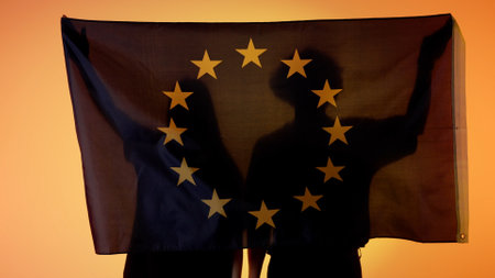 Silhouettes of people holding large flag on yellow background. Silhouettes of a man and a woman...