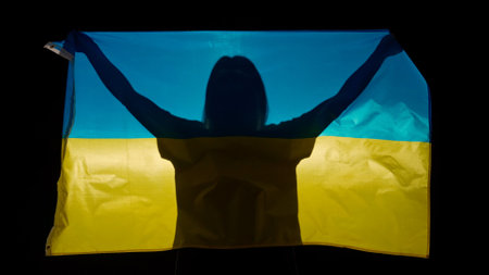 Person silhouette holding big flag against black background. Silhouette of woman with national flag...