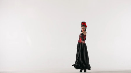 Woman dancer dancing on white background. Female in flamenco style dress performs elegant spanish dance moves with her hands and body in the studio.の写真素材