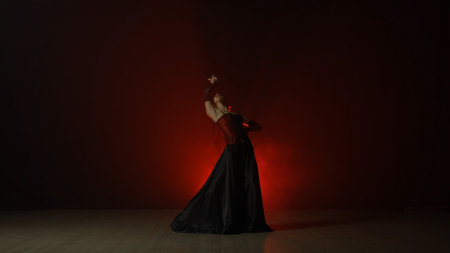 Woman dancing on black background with red light and smoke. Spanish dancer in red and black dress demonstrates elements of flamenco choreography.の写真素材