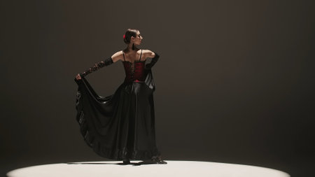 Woman dancing on black background under spotlights. Spanish dancer in red-black dress dancing elements of passionate flamenco.の写真素材
