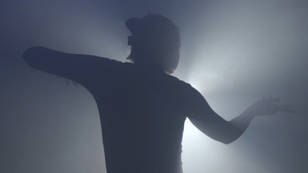 Female model against bright backlight on black smoky background in studio. Female silhouette, moving hand playing with a beam of light in the dark.の写真素材