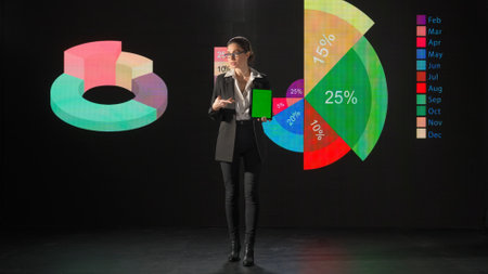 Woman presenting project on stage during meeting. A businesswoman talks to the audience, shows infographics, revenue analysis on a huge LED screen.の写真素材