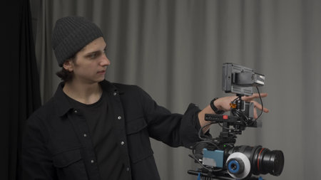 The operator adjusts a professional video camera standing on a tripod close up. Behind the scenes of...