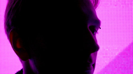 Male against big digital wall. Man face silhouette close up shot in front of digital screen wall with neon symbols in dark club.の写真素材