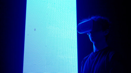 Man silhouette in virtual reality glasses standing in front of digital screen wall with neon symbols looking around playing video game.の写真素材