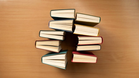 An overhead view of rows of books with colored covers on a wooden table.