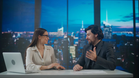 Male and female presenters in the studio. Man and woman news hosts sit at desk presenting evening...