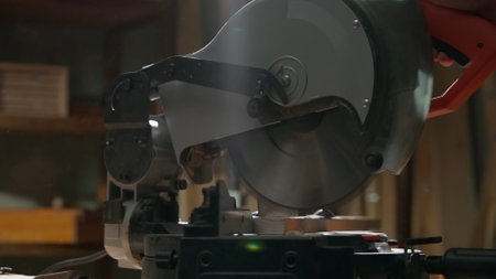 Male woodworker working in garage. Man professional carpenter specialist working with wooden materials in workshop, using circular saw to cut plank.の写真素材