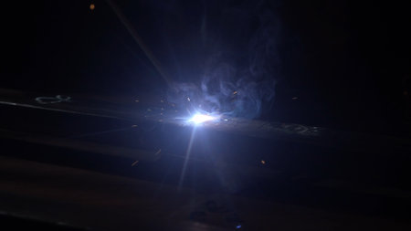 Metalworker using welding machine on iron surface, flame, sparks and flashing lights, close up view...