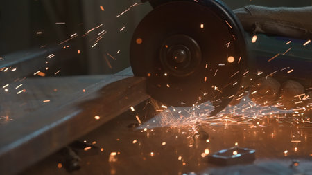 Craftsman in protective gloves working with grinder at industrial plant, man grinding iron detail, sparks flying around, view from glass sheet.の写真素材
