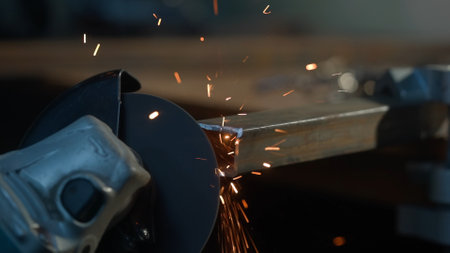 Craftsman working with grinder at industrial plant, man grinding edge of iron detail, sparks flying around and falling on the ground in workshop.の写真素材