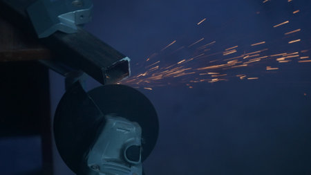 Craftsman working with grinder at industrial plant, man grinding iron detail, sparks flying around and falling on the ground in dark workshop. Close up shot.の写真素材