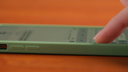 A hand types a message on a smartphone screen on a wooden table