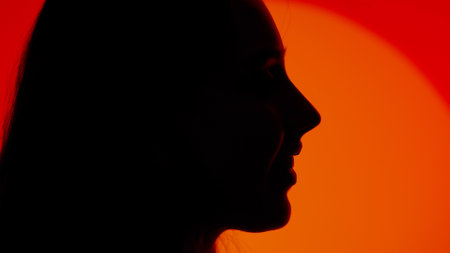 Stylish young woman black silhouette smiling positive profile face expression, close up shot. Isolated on red studio background spotlight.の写真素材