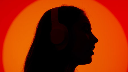 Stylish young woman black silhouette listening music in headphones, face close up. Isolated on red studio background spotlight.の写真素材