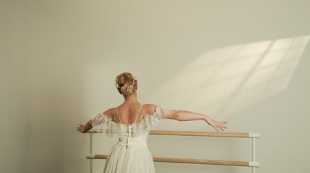 Ballet Dancer in White Dress Embracing Light at the Barreの写真素材