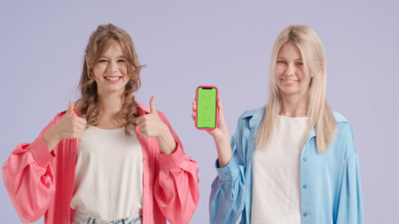 Young stylish women models holding pointing at smartphone chroma key green screen, isolated on purple background. Fashion and youth beauty concept.の写真素材