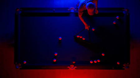 Hobby and leisure concept, billiard club scene shot. Top view of Russian billiard table in neon blue red light, man playing billiards.の写真素材