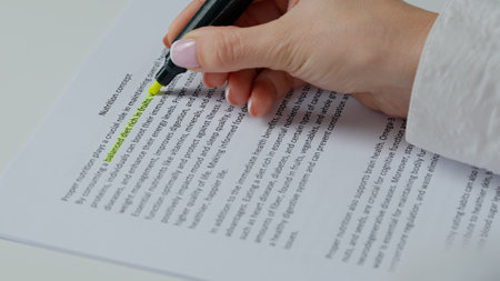 Close up shot of woman hand working with document, yellow marker in female hand marked highlighted an important parts in text.の写真素材