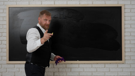 Man college teacher in classroom in front of chalkboard explaining lesson for students, writing formulas on board. Education concept.の写真素材