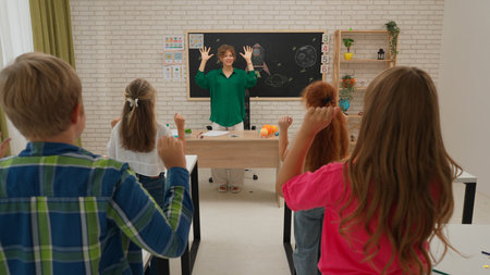 Junior school boys and girls sit in room in astronomy class. Female teacher and kids doing warm up...
