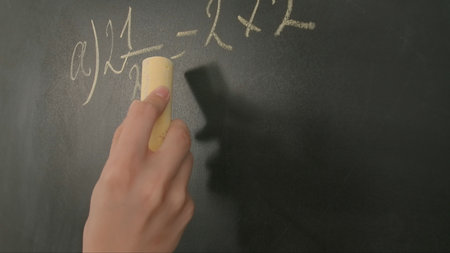 Close up of woman hand writing math sample and formula on chalkboard, professor writes on blackboard...