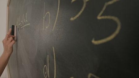 Close up of woman hand wiping algebra formulas task on chalkboard, professor writes on blackboard or...