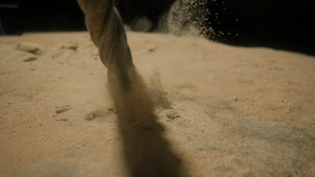 Close up of Drill Bit Penetrating Sand Surface with Dust Flyingの写真素材
