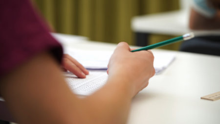 High school teenagers in classroom, close up shot boy writing math exam, solving task on paper sheet. Modern education concept.の写真素材